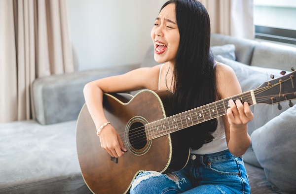 An Asian female guitarist is playing guitar lessons at home